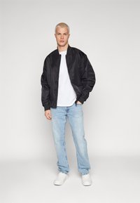 Black satin bomber jacket with elastic cuffs, worn over a white t-shirt, paired with light blue jeans and white sneakers. Simple, clean design.