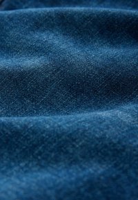 Nærbillede af tekstureret blåt denimstof med synligt diagonalt vævemønster og bløde folder.