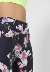 Legíny s vysokým pasem mají květinový vzor v odstínech růžové a bílé na tmavém pozadí, vyrobené z elastického a texturovaného materiálu.