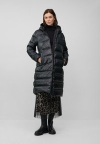 Zwarte pufferjas met een capuchon en een voorkant rits, met een glanzende afwerking, een gevoerd ontwerp en zakken aan de zijkant. Gecombineerd met een rok met luipaardprint.