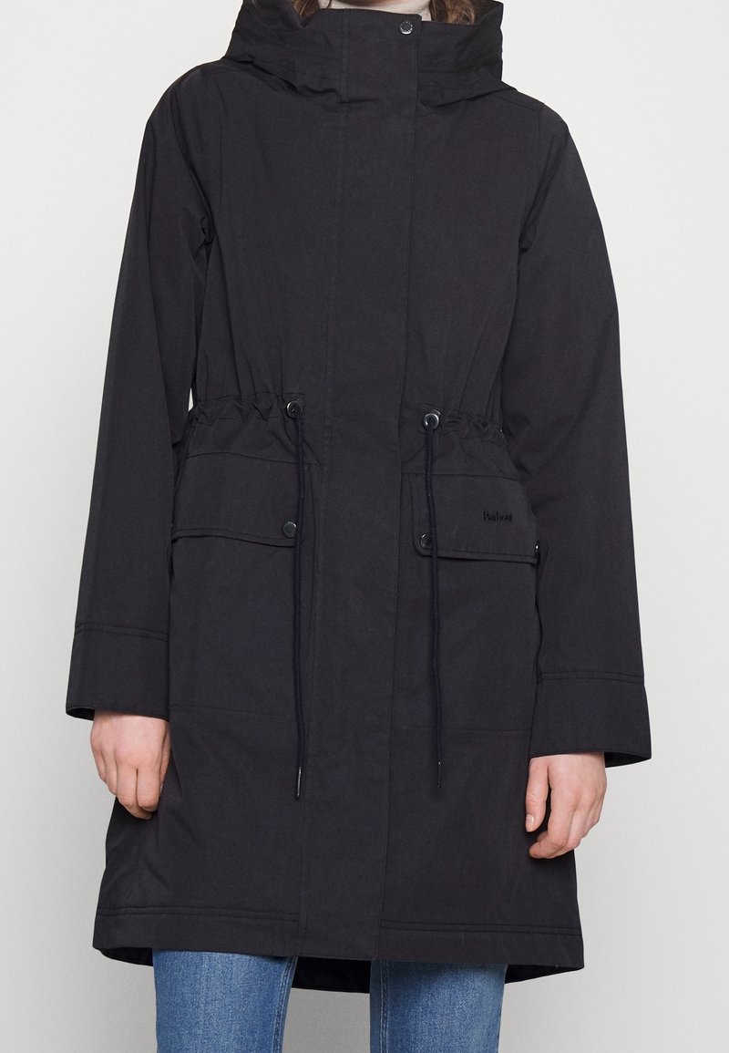 Black parka coat with a hood, drawstring waist, large front pockets, and snap closures. Made from a smooth, water-resistant material.