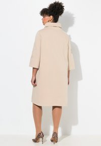Beiges Kleid mit Kapuze und dreiviertel Ärmeln, glatte Textur, knielang, kombiniert mit spitzen, leopardmusternden High Heels.