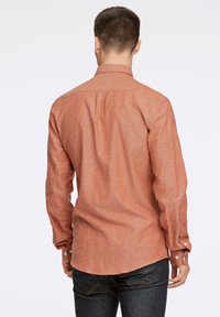 Camicia a maniche lunghe color ruggine con una trama texturizzata, polsini a bottoni e orlo curvo, progettata con un dettaglio a yoke sul retro.