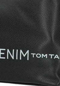 Bolso de cuero negro texturizado que presenta los logotipos en relieve "DENIM" y "TOM TAILOR". El diseño es sencillo, con un acabado liso y un brillo sutil.