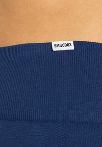 Granatowy prążkowany materiał o gładkiej fakturze; posiada biały metkę z napisem "SMILODOX" przy pasie.