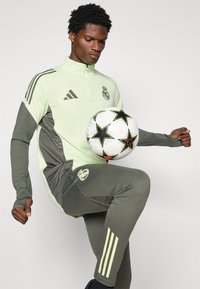 Trainingsanzug aus hellgrünem und grauem Stoff mit langen Ärmeln und hochgeschlossenem Kragen. Verfügt über schwarze Adidas-Streifen und einen Fußball mit Sternmuster.