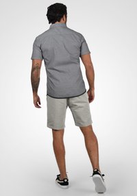 Chemise grise à manches courtes avec une texture subtile, associée à un short gris clair. La tenue se compose de shorts retroussés et de baskets noires.