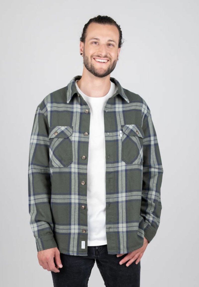 Groene en grijze geblokte shirt van stof, met twee borstzakken, knoopsluiting en een wit onderhemd.