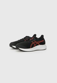 Chaussures de sport noires avec une tige en mesh, ornées d'accents rouges et d'une semelle blanche. Design minimaliste avec un bout rond et un système de laçage.