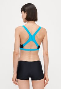 Haut de bain sportif avec un design à dos croisé, des bretelles larges turquoise, un corps noir et un short noir ajusté. Texture lisse, détails minimaux.