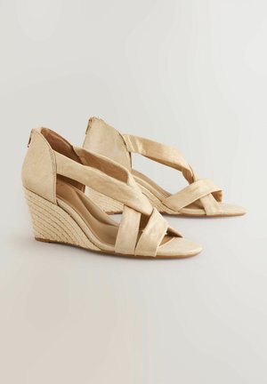 Beige wedge sandals with a crisscross strap design, suede-like texture, and jute-wrapped heel. Open toe and back heel coverage.