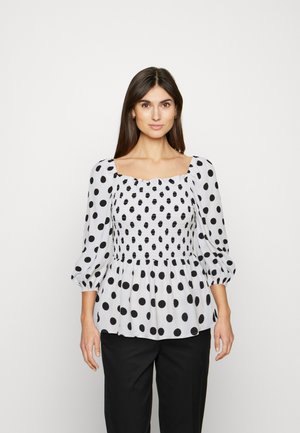 Blusa branca com bolinhas pretas, decote quadrado e corpete franzido. Apresenta mangas bufantes e um detalhe em bainha evasé.
