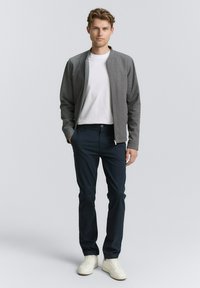 Szara kurtka bomberka, biała koszulka, granatowe spodnie i białe trampki. Kurtka ma przedni zamek błyskawiczny, prążkowane mankiety oraz luźny krój.