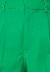Calças verdes sob medida feitas de tecido texturizado, com frente lisa, fecho de correr e detalhes de costura intrincados ao longo das costuras.