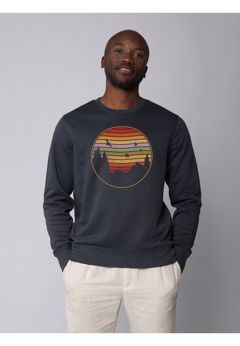 Sweatshirt en coton bleu marine à manches longues, avec un motif circulaire de coucher de soleil dans des teintes d'orange, rouge et jaune, et une silhouette noire d'arbres.