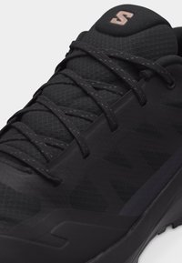 Černá sportovní obuv s horní částí z mesh materiálu, černými tkaničkami a značkovým logem na polstrovaném jazyku, s texturovanými a hladkými syntetickými překryvy.