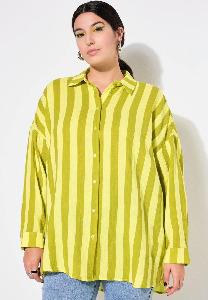 Camicia a maniche lunghe in tessuto verde chiaro con strisce verticali gialle. Chiusura frontale con bottoni, vestibilità rilassata e polsini larghi.