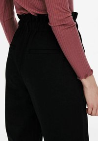 Zwarte high-waisted broek met een gathered elastische tailleband en zijzakken, gecombineerd met een aansluitend geribd bordeauxrood topje.