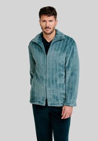 Chaqueta de forro polar turquesa con rayas verticales, cierre con cremallera en la parte frontal, cuello alto y textura suave, combinada con pantalones oscuros.