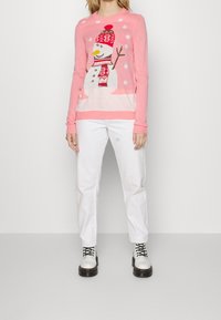 Rosa Pullover mit einem Schneemann-Design, der einen Hut und einen Schal trägt; weiße Hose; schwarz-weiße Stiefel; glatte Textur; verspieltes Winterthema.