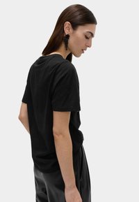 Černé bavlněné tričko s krátkým rukávem, volnější střih a kulatým výstřihem, kombinované s lesklými černými kalhotami s vysokým pasem.