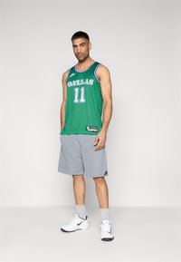 Πράσινη μπασκετική φανέλα με το κείμενο "DALLAS", αριθμός 11, σετ με γκρι σορτς, λευκά αθλητικά παπούτσια και γκρι κάλτσες. Ελαφρύ ύφασμα, αθλητική εφαρμογή.