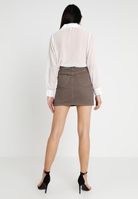 Blusa bianca trasparente a maniche lunghe con collare e gonna mini a quadretti neri e marroni con tasche, abbinata a tacchi neri.