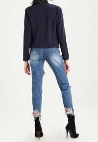 Námořnicky modrý krátký blejzr s dlouhými rukávy, doplněný roztrhanými světlými modrými džínami. Černé kotníkové boty na vysokém podpatku dokončují outfit.