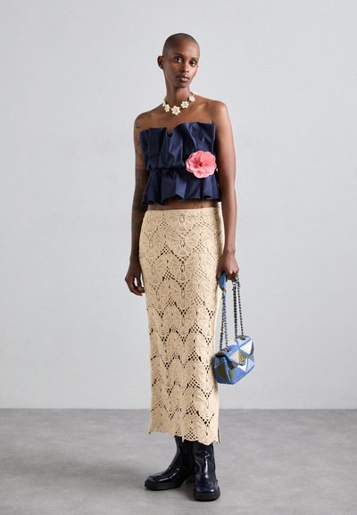Navy ruffled crop top with a pink flower, beige crochet maxi skirt, blue geometric handbag, and knee-high black boots.