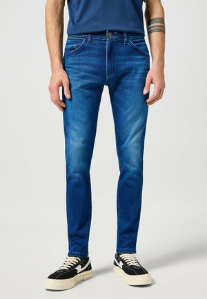 Blaue Jeans im Slim-Fit-Stil mit klassischem Fünf-Taschen-Design und dezentem Verblassen. Kombiniert mit schwarz-weißen Sneakers.