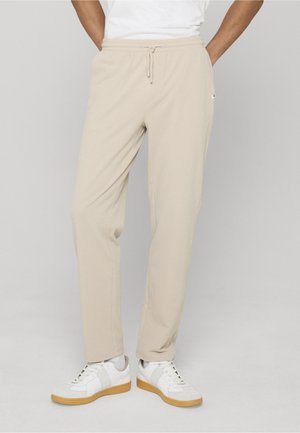 Pantaloni jogger beige texturizzati con vita regolabile a coulisse e tasche laterali, abbinati a sneakers bianche con suola in gomma color caramello.