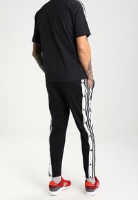 Svart träningsset bestående av en kortärmad topp och smala byxor med vita sidostickningar och tryckknappsdetaljer. Röda sneakers fulländar looken.