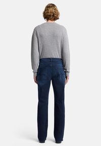 Pullover grigio a maniche lunghe abbinato a jeans blu scuro a gamba dritta, con tasche posteriori e dettagli di cucitura sottili.