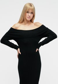 Vestito nero scollato con maniche lunghe, tessuto a coste, design aderente e taglio a metà lunghezza. Tessuto morbido ed elastico.