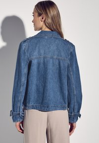 Denimjacka i blekt blå med avslappnad passform, axelstycken, elastisk nederkant och justerbara ärmslut. Slät textur med synlig sömnad.
