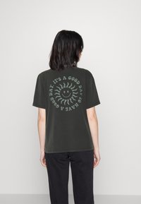 Persona con cabello oscuro que lleva una camiseta negra con un sol sonriente y el texto "Es un buen día para tener un buen día" en la parte de atrás.