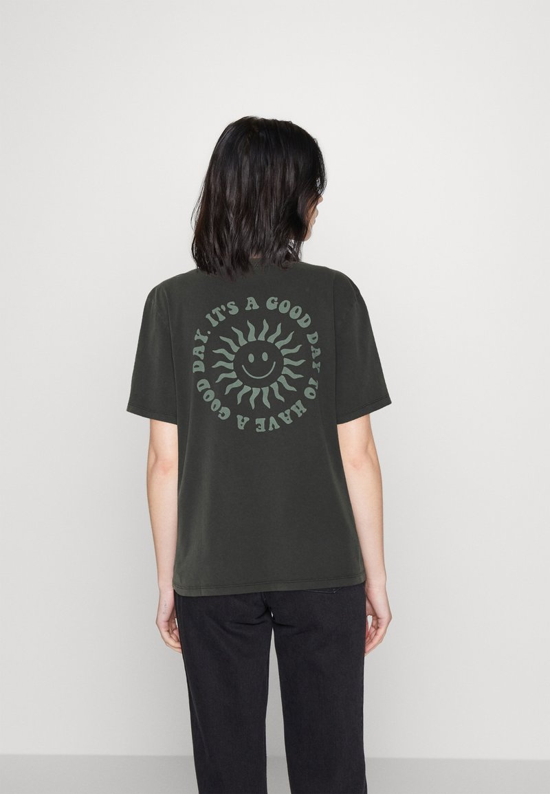 Persona con cabello oscuro que lleva una camiseta negra con un sol sonriente y el texto "Es un buen día para tener un buen día" en la parte de atrás.