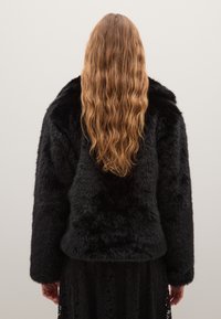 Giubbotto in pelliccia sintetica nera con una superficie spessa e testurizzata e una vestibilità comoda. Presenta maniche lunghe e un design con spalle arrotondate.