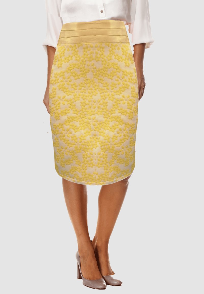 Mujer que lleva una falda lápiz texturizada floral amarilla con una cintura ancha, combinada con unos tacones altos color topo y una blusa blanca.