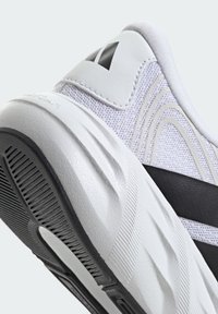 Talons de chaussure de sport blanc et noir montrant une semelle texturée, une tige en maille et un logo noir partiel sur fond blanc.