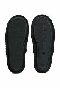 Zapatos negros sin cordones con una suela de goma texturizada, que presentan un branding sutil. La parte superior está hecha de una tela suave con un diseño simple.