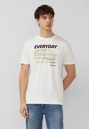 Mężczyzna noszący białą koszulkę z napisem „EVERYDAY” oraz słowami „FEEL OBSERVE GROW RETHINK Reflect&Act” nadrukowanymi, w połączeniu z niebieskimi dżinsami.