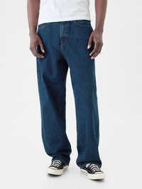 Pantalones vaqueros de pierna ancha en azul oscuro, hechos de denim, con un clásico diseño de cinco bolsillos y detalles de costura mínimos, usados con zapatillas negras.