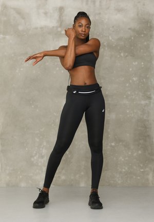 Sujetador deportivo negro y leggings ajustados hechos de un material elástico, combinados con zapatos deportivos negros. Cuenta con un pouch con cremallera en la cintura para almacenamiento.