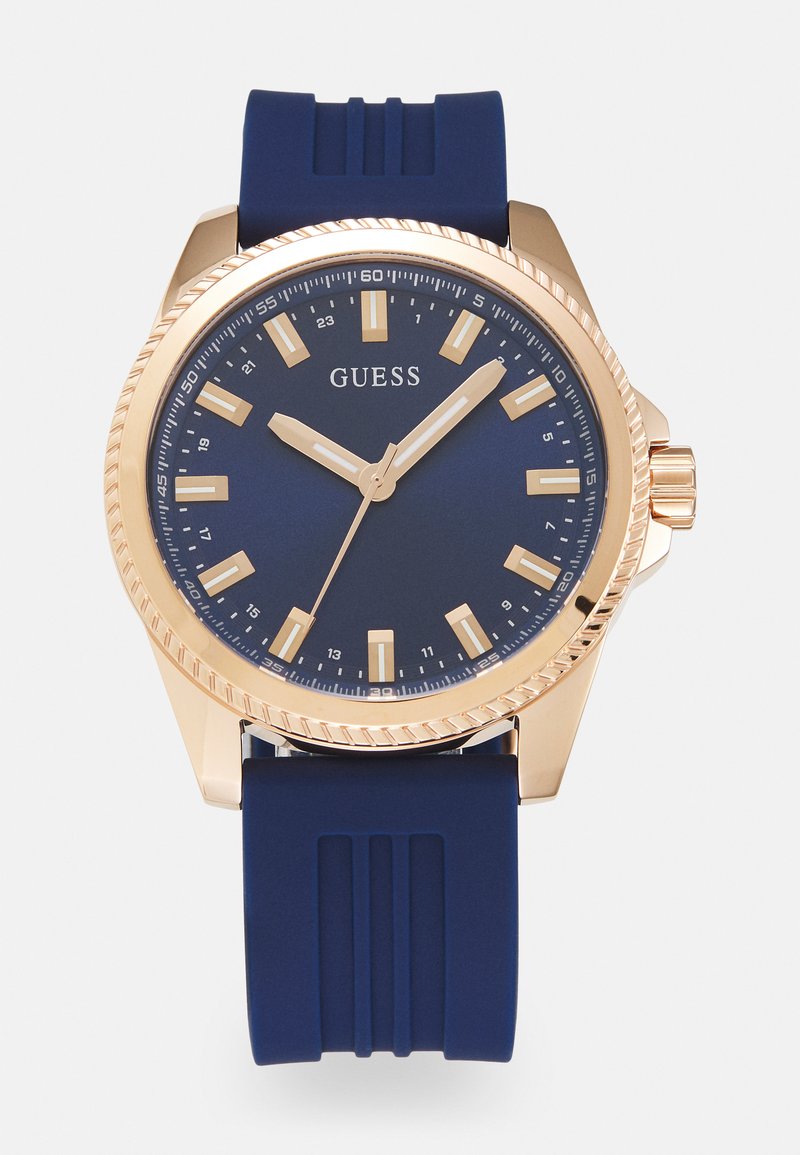 Montre avec bracelet en silicone marine, boîtier en acier inoxydable doré, cadran bleu foncé, index heures dorés et couronne texturée.
