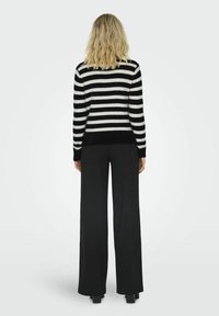 Pull rayé noir et blanc avec une texture douce, associé à un pantalon noir à jambes larges et taille haute, vu de dos.