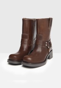 Bruine leren enkelboots met een ronde neus, ritsluiting en een decoratieve band met metalen accenten. Stevige blokhak.