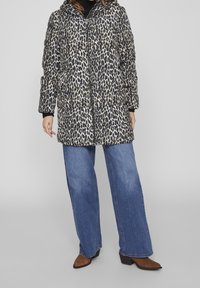 Chaqueta acolchada de estampado de leopardo con capucha, cierre de cremallera y textura acolchada; combinada con vaqueros de pierna ancha en azul y botas de tacón marrones.