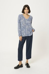 Blouse bleu à manches longues avec un motif de feuilles blanches, décolleté en V et coupe décontractée, assortie à un pantalon bleu marine et des mocassins noirs.