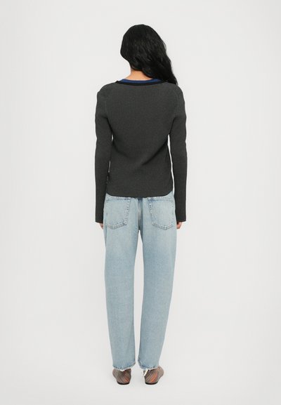 Pullover a costine grigio scuro con maniche lunghe, abbinato a jeans larghi di colore blu chiaro. Scarpe slip-on con strisce colorate.